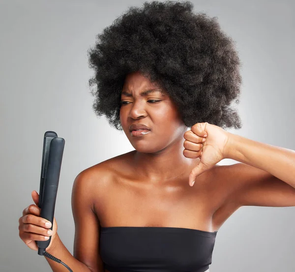 We dont use this around here. a young woman showing a thumbs down while holding a hair product against a grey background