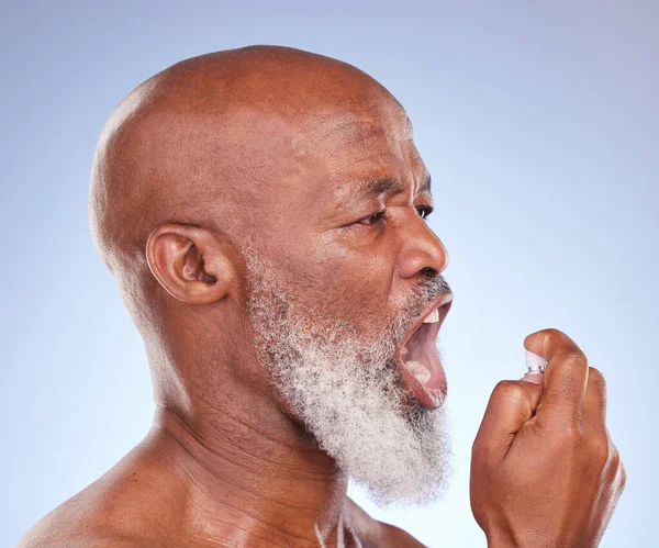 Quick fixes and busy lives. Studio shot of a mature man checking his breath and using breath freshening spray against a blue background