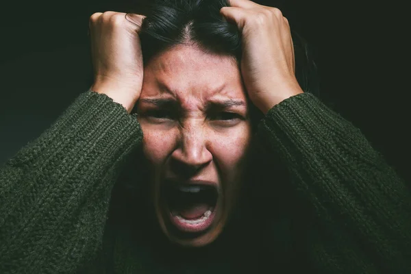 Is it all in your head. Studio shot of a young woman experiencing mental anguish and screaming against a black background