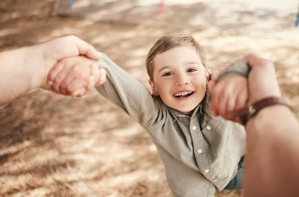 Close up face of happy caucasian boy swinging and spinning in circles by the arms at the park with his father. Cute playful kid having fun while bonding with a parent on a sunny summer outdoors.