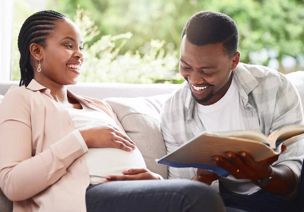 Story time. a handsome young man reading a book to pregnant wifes belly while sitting on the sofa at home