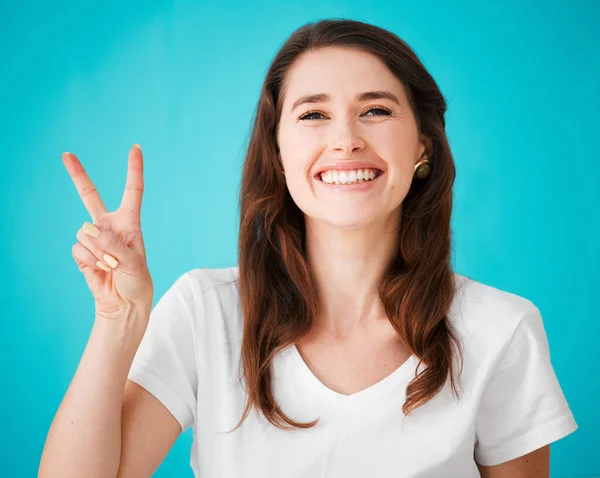 Peace, love and positivity. Studio portrait of an attractive young woman showing the peace sign to the camera against a blue background