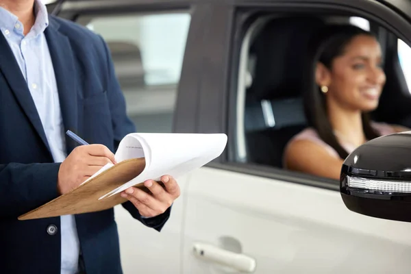 Another day, another car sold. a man filling in paperwork while standing next to a woman in a car