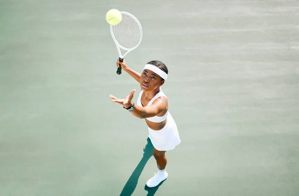 Theres power in her swing. a young woman serving a ball while playing tennis on a court
