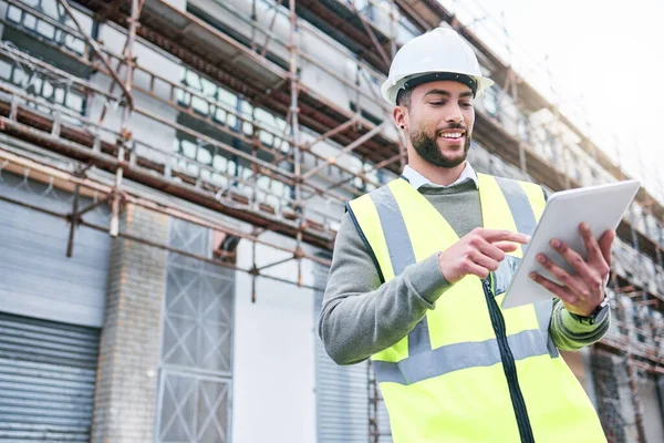 Success is a personal standard. a handsome male construction worker using a tablet while standing outside