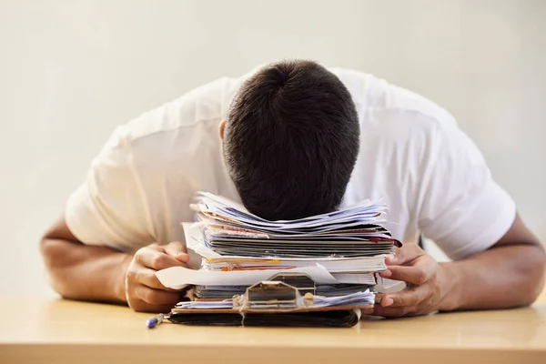 I cant cope with all of this work. an unrecognisable man asleep on a stack of paperwork while working from home