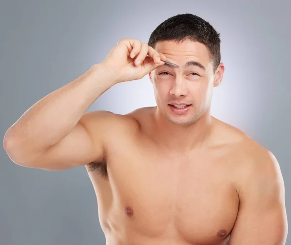 I prefer the clean look. a handsome young man tweezing his eyebrows