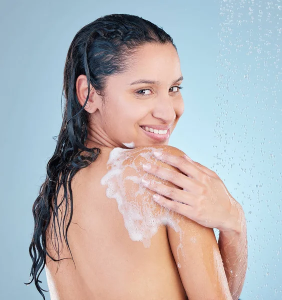 I might need help reaching my back. Studio shot of an attractive young woman taking a shower against a blue background