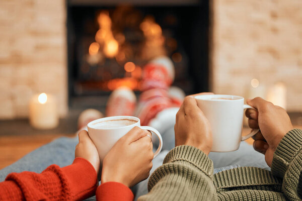Hot cocoa just tastes better this time of year. Closeup shot of a couple having warm drinks while relaxing by a fireplace at home