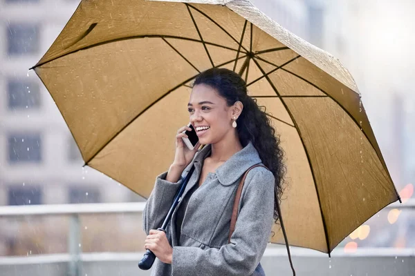 Im caught in the rain. a young woman holding an umbrella while on a call in the rain