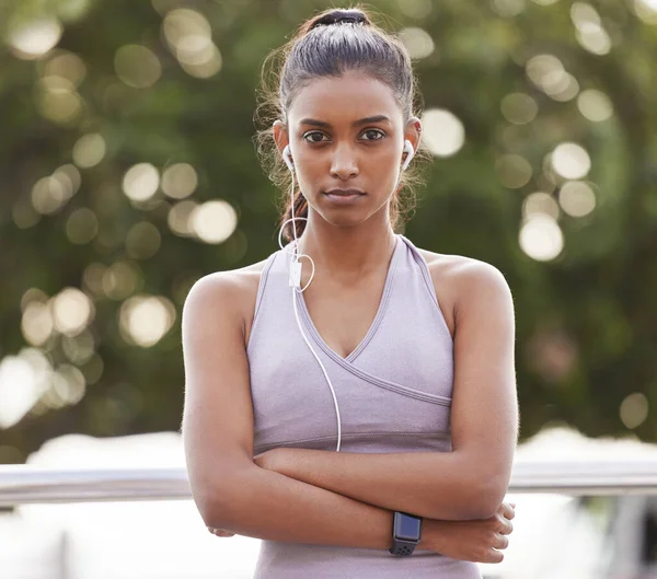 You wont go anywhere without determination. Portrait of a sporty young woman wearing earphones and standing with her arms crossed while exercising outdoors