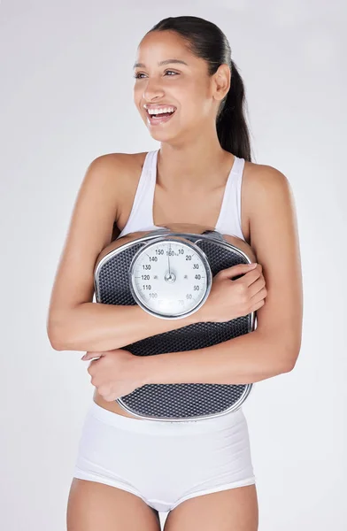 She couldnt be happier. Studio shot of an attractive young woman posing with a weightscale against a grey background