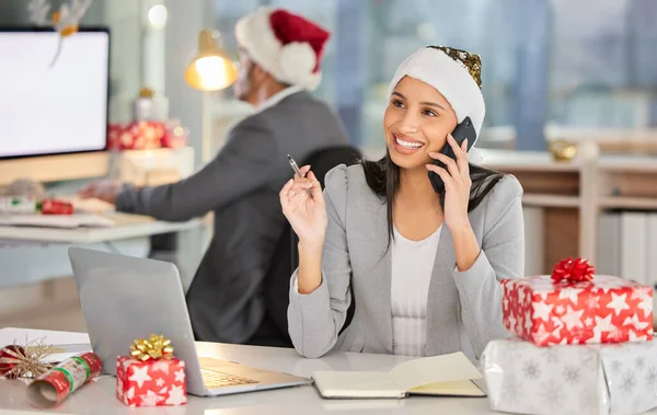 Christmas is here and the office is filled with cheer. a young businesswoman using a laptop and smartphone in a modern office at Christmas