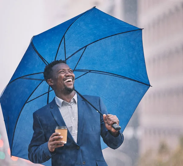 This is definitely my kind of weather. a young businessman holding an umbrella in the rain against a city background