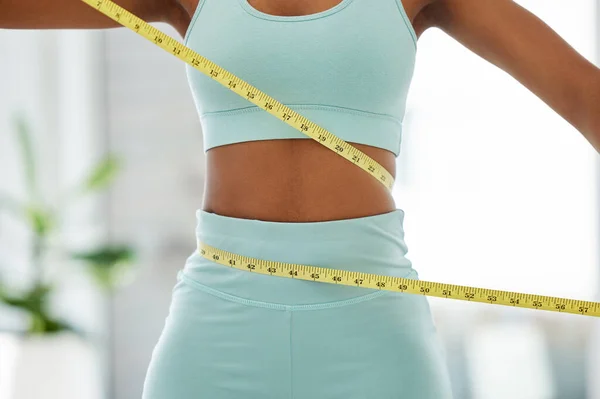 Losing those pounds. an unrecognisable woman standing alone and using a measuring tape around her waist in a yoga studio