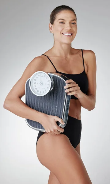 Scale down on bad food, beef up on the good. Studio shot of an attractive and fit young woman holding a scale against a grey background