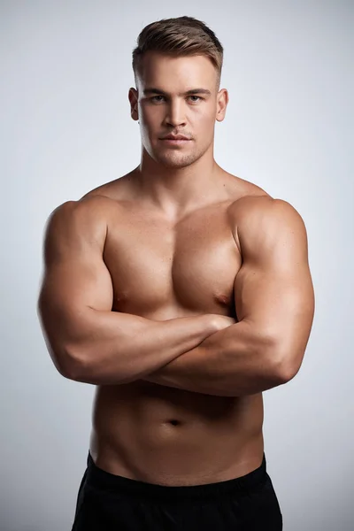 Your body is a strong machine. Studio portrait of a muscular young man posing with his arms crossed against a grey background