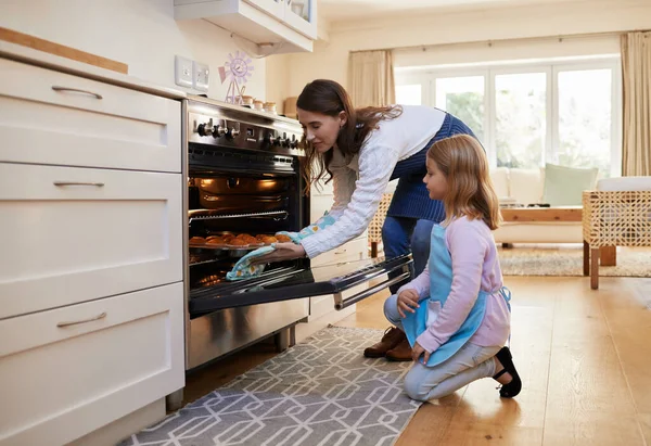 Always get an adult to help you. a mother and daughter inserting a tray of cupcakes into the oven