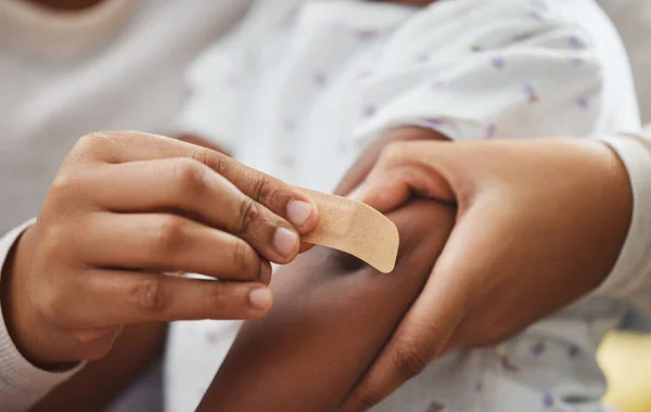 This will make it better. an unrecognizable mother applying a bandaid to her daughters arm at home