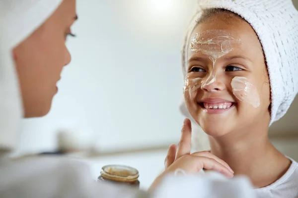 Cute, happy and little girl doing beauty treatment together with her mother. Daughter getting a facial and smiling in the bathroom at home. Adorable child copying her mom, bonding and smiling inside.