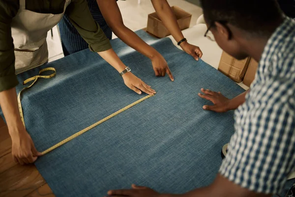 Fashion, design and style with a professional team measuring fabric in a creative textile workshop from above. A tailor and his colleagues creating trendy, fashionable clothing in a factory.