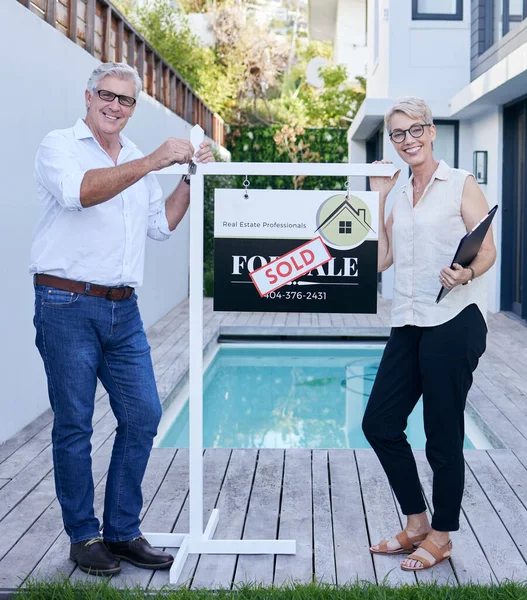 Finding the perfect retirement home. Cropped portrait of a mature couple holding their keys while standing in front of a for sale board with a sold sticker on it