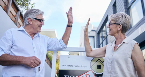 Selling houses is what they do. Low angle shot of two mature people high fiving while standing in front of a for sale board with a sold sticker on it