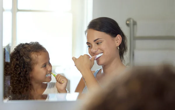 Dental care, brushing teeth and healthy routine in mother and daughter morning at home. Happy, fun and playful child and parent bonding and learning hygiene and grooming with toothpaste in a bathroom.