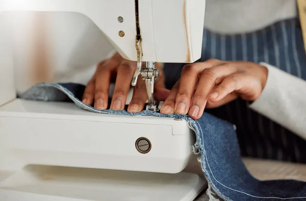 Close up hands of a professional female designer sitting on a sewing machine in her studio. Process of a tailor at work on repairing and designing clothes. Casual alterations being done to jeans