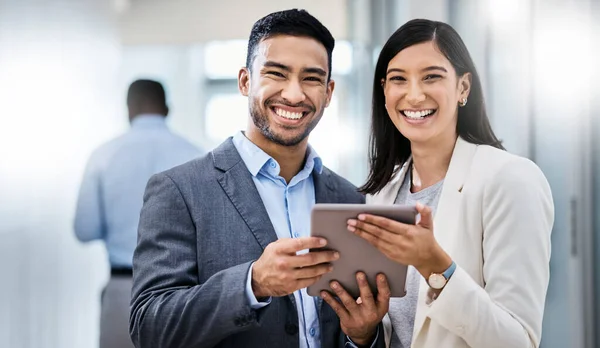 Follow us to learn more about what we do. two businesspeople standing together and holding a digital tablet in an office