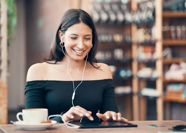 Beautiful, happy and relaxed student listening to a podcast, education video or music in cafe on a tablet. Smiling woman browsing online and watching distance learning webinar in restaurant.
