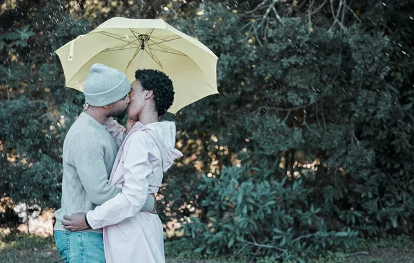 The best kisses are the ones shared in the rain. a young couple kissing while standing under an umbrella