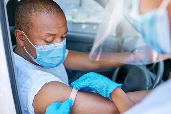 Mobile covid vaccine service outdoors for a patient driving in a car. A healthcare professional applying a plaster on a patient in a vehicle after coronavirus treatment at a vaccination station.