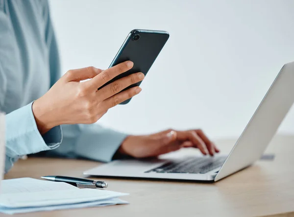 Modern businesswoman texting on phone and laptop while working, reading and planning strategy indoors. Closeup of a productive corporate worker multitasking on multimedia technology and app software.