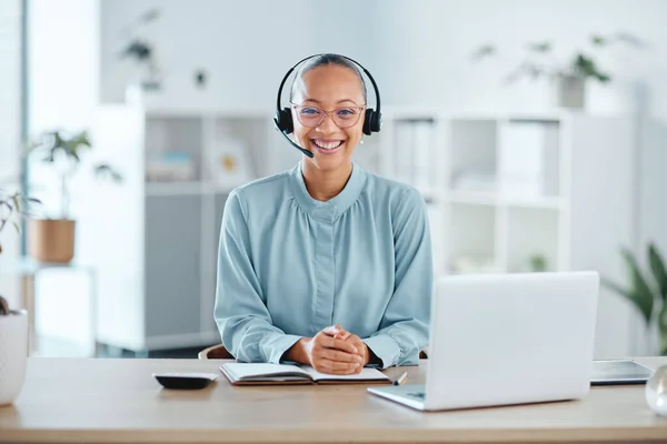 Happy and confident call center agent sitting in front of a laptop while wearing a headset in an office. Portrait of a cheerful saleswoman using web chat to assist customer sales and service support.