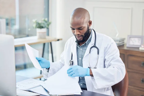 Where on earth did I put that prescription. a handsome young doctor sitting alone in his clinic and reading paperwork