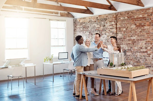 Team of happy architect engineers celebrating together with a high five after completing a small apartment complex model to scale. Group of professional designers design a blueprint office building.