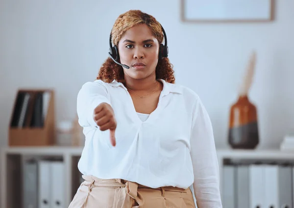 Thumbs down from call center agent, annoyed and angry while wearing a headset. Portrait of a young woman feeling the pressure of a bad workplace, frustrated and unhappy at her job, work environment.