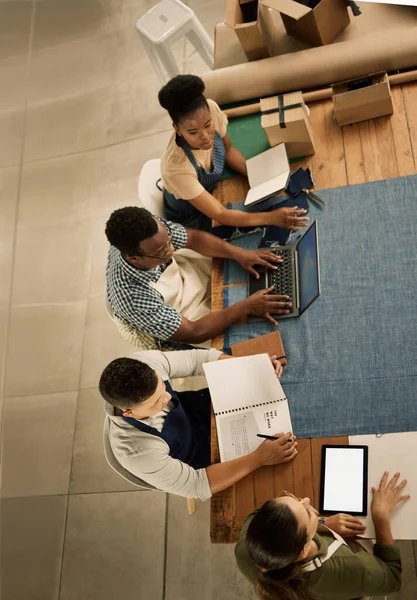 Group of fashion designers talking, planning and discussing creative strategy in meeting at a textile, manufacturing or tailor shop from above. Design professionals brainstorming and working on tech.