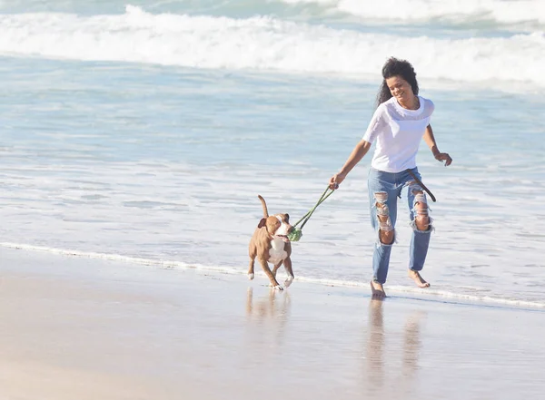 The best things in life are furry. a woman playing with her pit bull at the beach