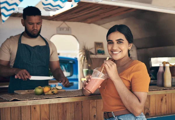 I come here every weekend. a woman buying and drinking a smoothie from a food truck