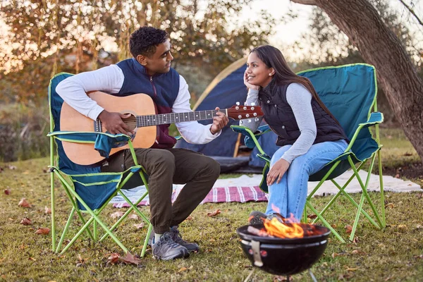 Live ,love ,laugh ,camp. a you man playing his guitar to his wife outside while camping