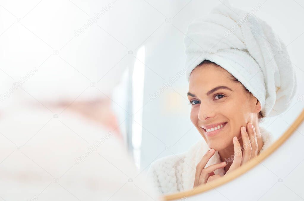 My skin has never looked better. a young woman analysing her reflection in her bathroom mirror