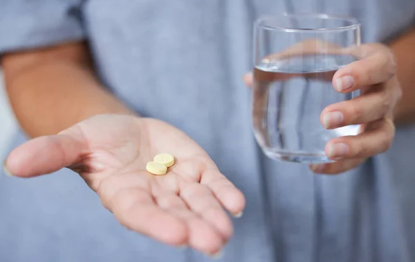 I take these daily. a senior woman holding a glass of water and two tablets