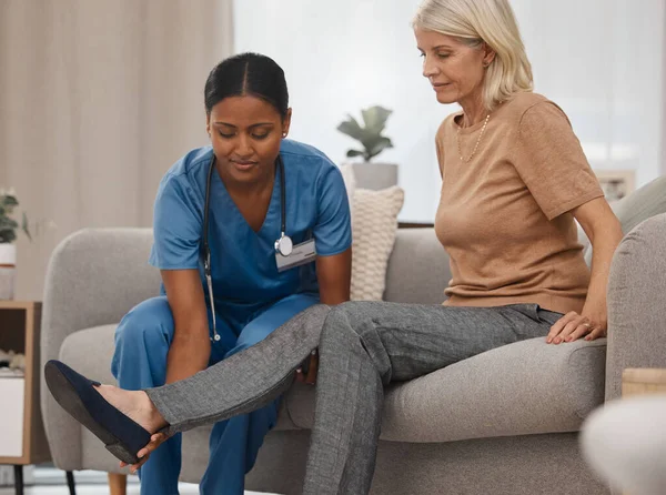 Does the pain feel worse when you flex your ankle. a doctor examining a senior womans ankle on the sofa at home