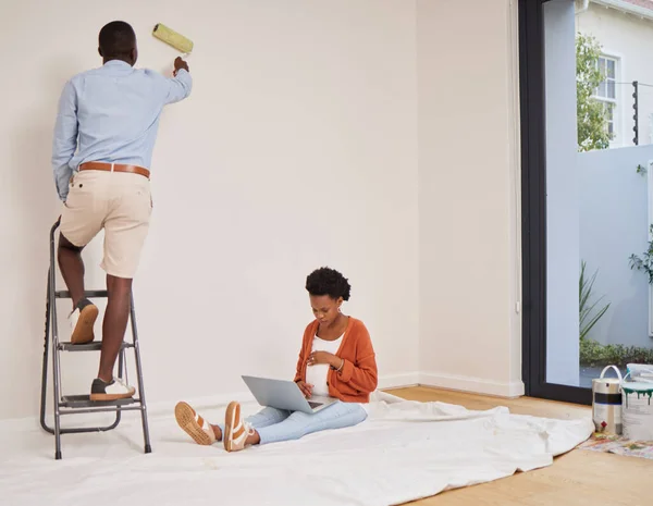 Taking the weight of my feet while he paints. Full length shot of a young couple redecorating a room at home with fresh paint