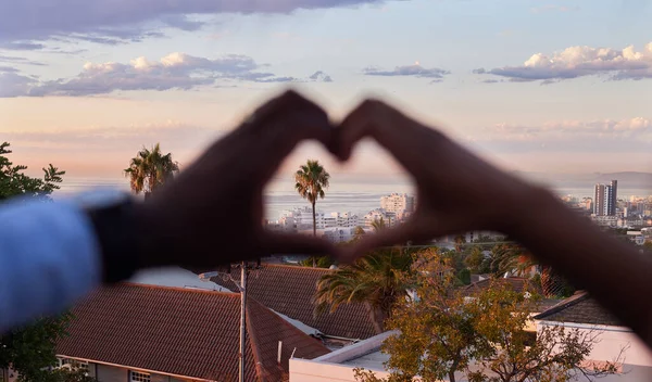 Living a life full of love. an unrecognizable couple making a heart shaped gesture with the city in the background