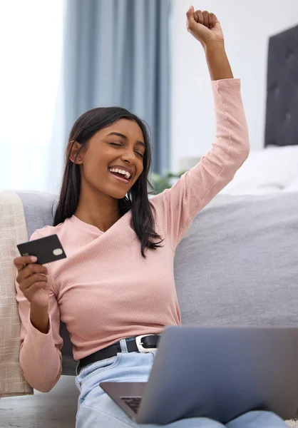 Ive just gotten the best deal. an attractive young woman cheering while holding a credit card and using her laptop in the bedroom at home