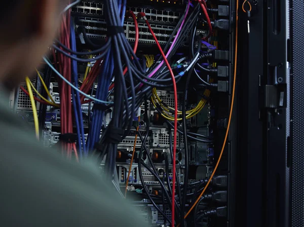 Lets organize this cabling. an unrecognizable male IT support agent working in a dark network server room