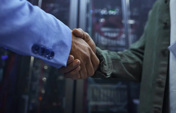 Happy to help. two unrecognizable male IT support agents shaking hands in a dark network server room